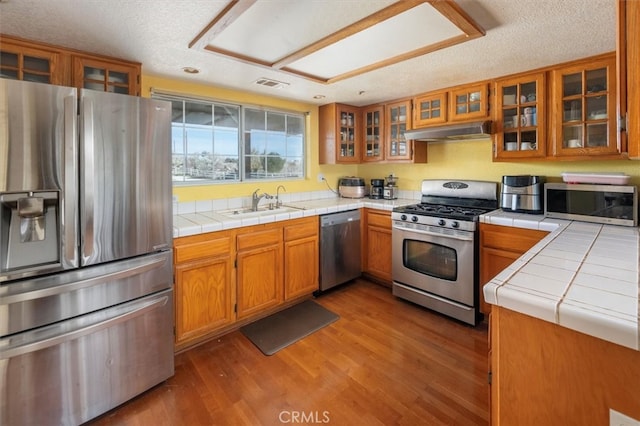 kitchen with appliances with stainless steel finishes, tile counters, a textured ceiling, and light hardwood / wood-style flooring