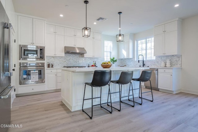 kitchen with white cabinets, a kitchen island, light wood-type flooring, and stainless steel appliances