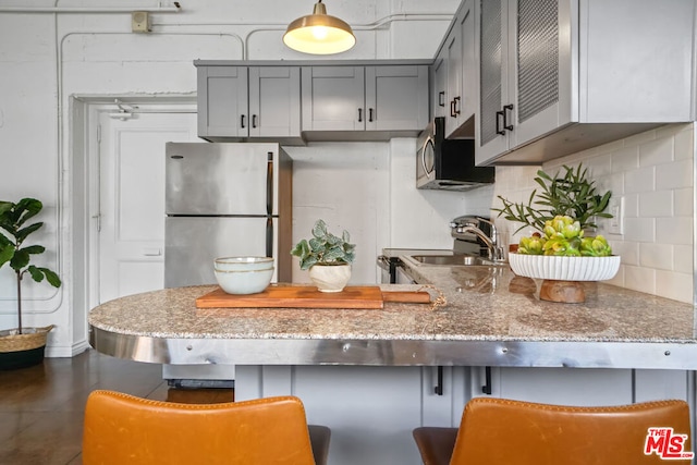 kitchen featuring light stone counters, pendant lighting, sink, gray cabinetry, and appliances with stainless steel finishes