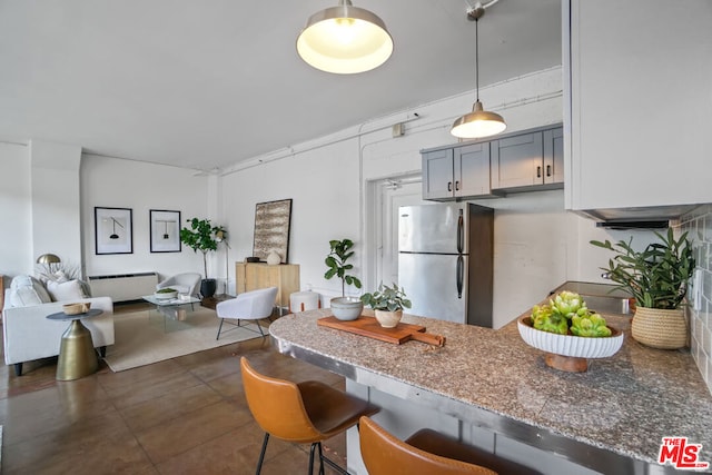 kitchen featuring stainless steel refrigerator, a kitchen bar, gray cabinetry, and kitchen peninsula