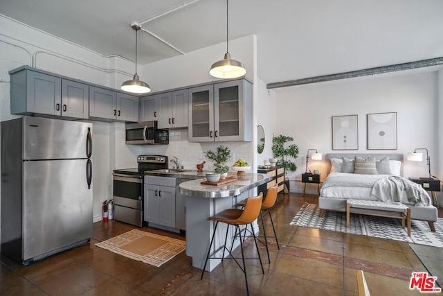 kitchen featuring appliances with stainless steel finishes, decorative backsplash, gray cabinetry, a kitchen bar, and decorative light fixtures