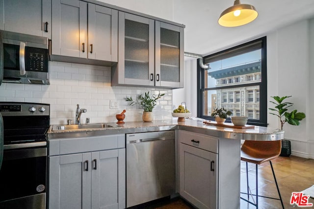 kitchen with sink, appliances with stainless steel finishes, kitchen peninsula, and gray cabinets