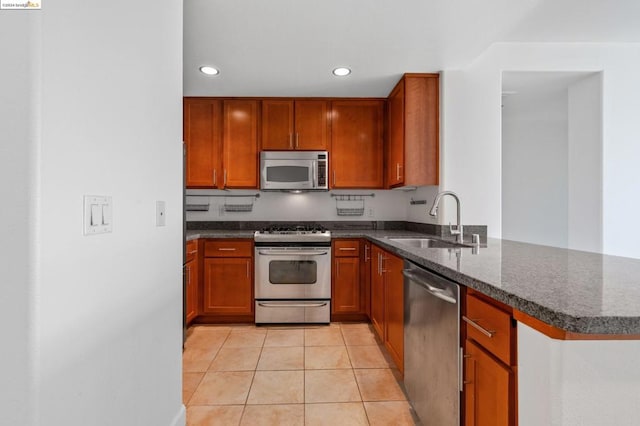 kitchen featuring appliances with stainless steel finishes, kitchen peninsula, light tile patterned floors, dark stone counters, and sink