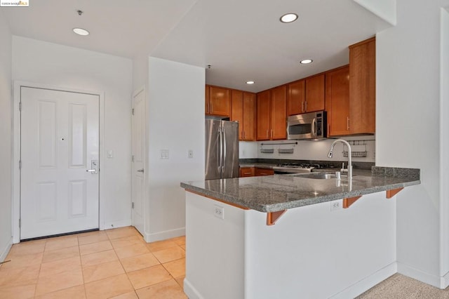 kitchen with dark stone counters, sink, kitchen peninsula, a kitchen breakfast bar, and appliances with stainless steel finishes