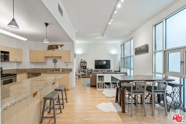 kitchen featuring light brown cabinetry, light hardwood / wood-style flooring, stainless steel appliances, light stone countertops, and hanging light fixtures