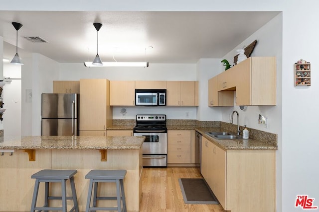 kitchen featuring light wood-type flooring, light brown cabinetry, decorative light fixtures, sink, and appliances with stainless steel finishes