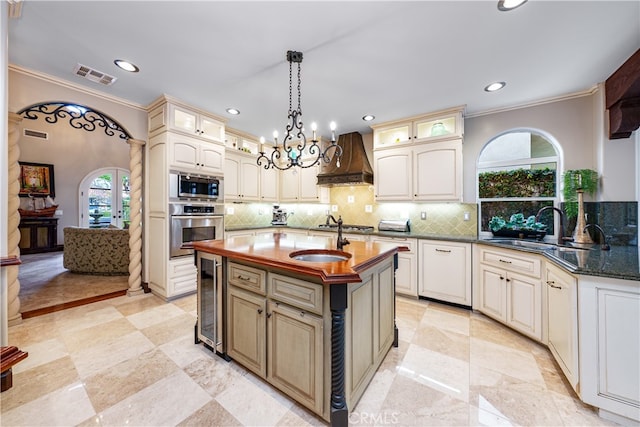 kitchen with plenty of natural light, appliances with stainless steel finishes, premium range hood, and an island with sink