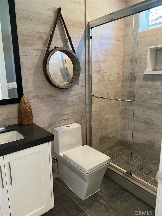 bathroom featuring vanity, a shower with door, tile walls, tile patterned flooring, and toilet