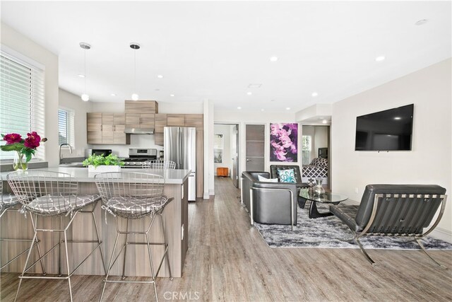 kitchen with sink, decorative light fixtures, stainless steel appliances, a breakfast bar, and light wood-type flooring