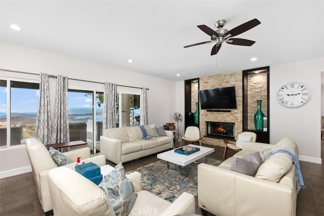 living room with ceiling fan, a stone fireplace, and dark wood-type flooring