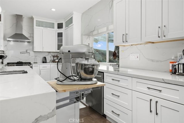 kitchen with wall chimney exhaust hood, light stone counters, white cabinetry, and tasteful backsplash