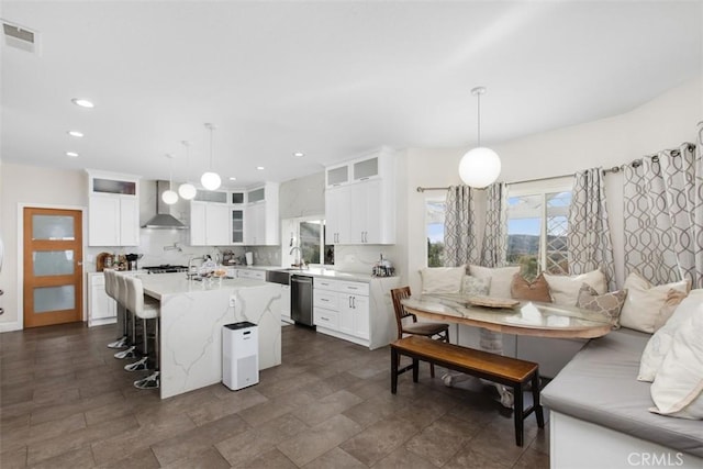 kitchen with white cabinetry, dishwasher, wall chimney exhaust hood, hanging light fixtures, and a kitchen island