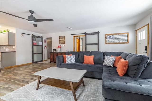 living room with ceiling fan, a barn door, and wood-type flooring