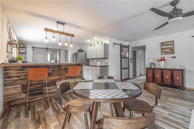 dining space with a barn door, ceiling fan, and light hardwood / wood-style floors