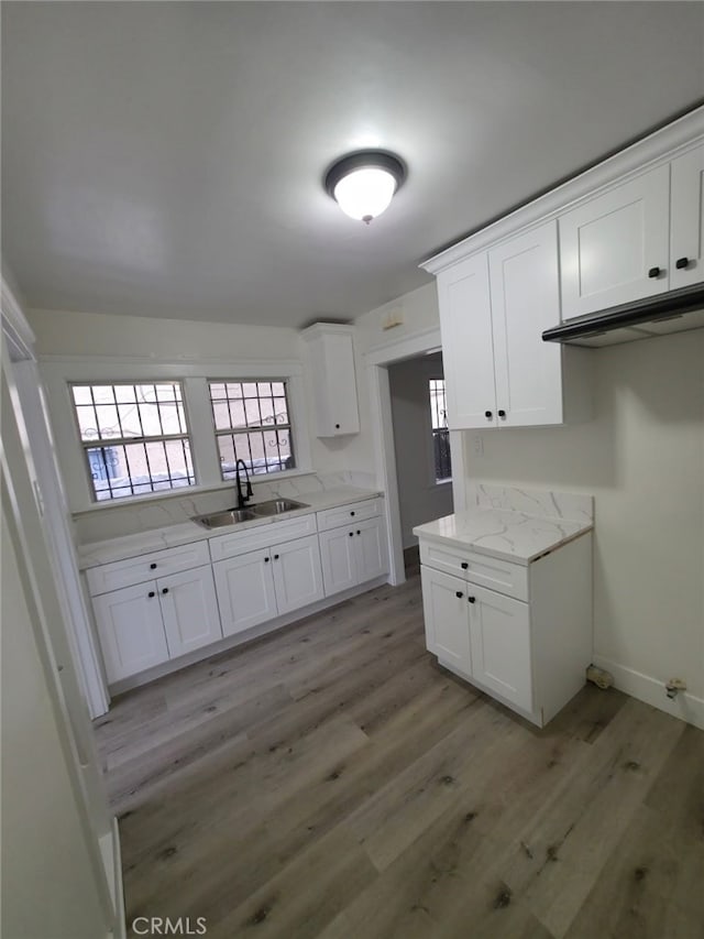 kitchen with light wood-type flooring, baseboards, a sink, light stone counters, and white cabinets