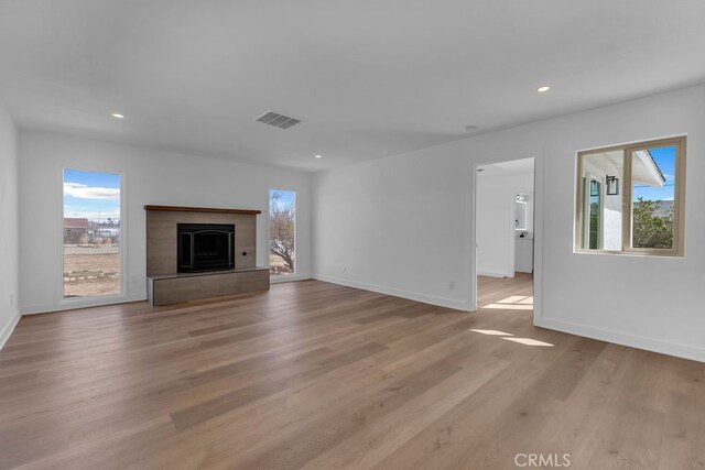 unfurnished living room featuring a tiled fireplace, light hardwood / wood-style floors, and plenty of natural light