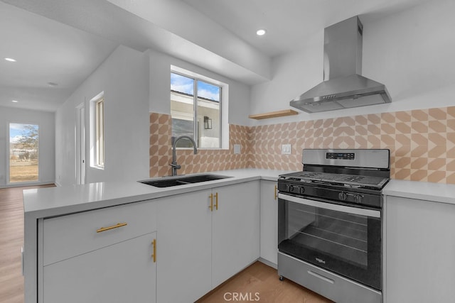 kitchen with decorative backsplash, wall chimney exhaust hood, stainless steel gas range, sink, and light hardwood / wood-style floors