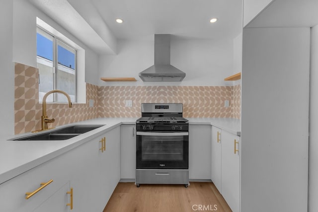 kitchen featuring gas range, wall chimney exhaust hood, white cabinets, and sink