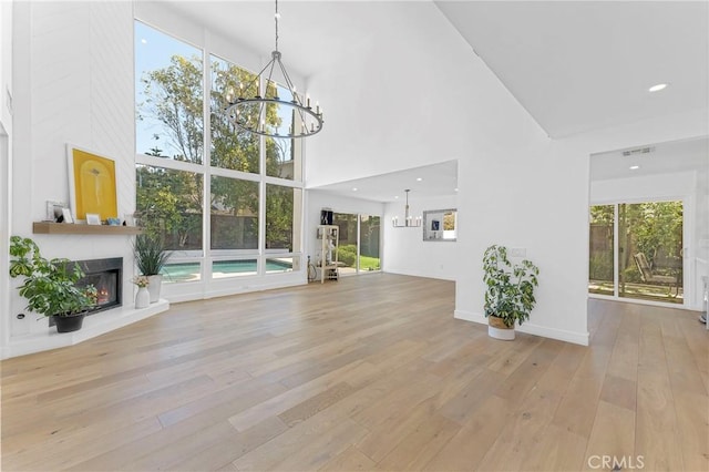 unfurnished living room featuring a fireplace, a towering ceiling, an inviting chandelier, and light hardwood / wood-style flooring