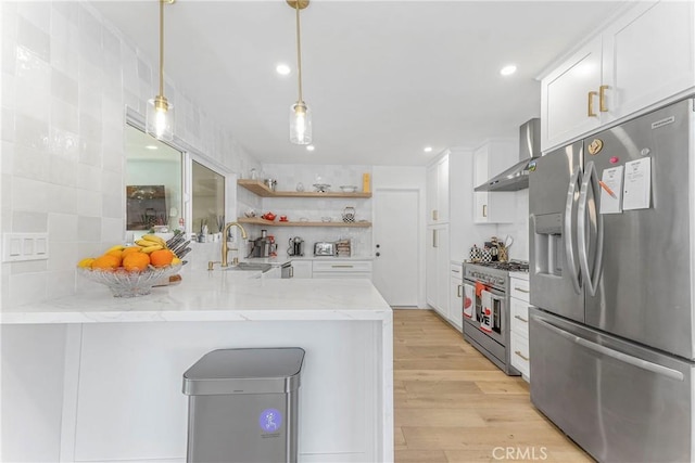 kitchen featuring kitchen peninsula, wall chimney exhaust hood, stainless steel appliances, sink, and pendant lighting