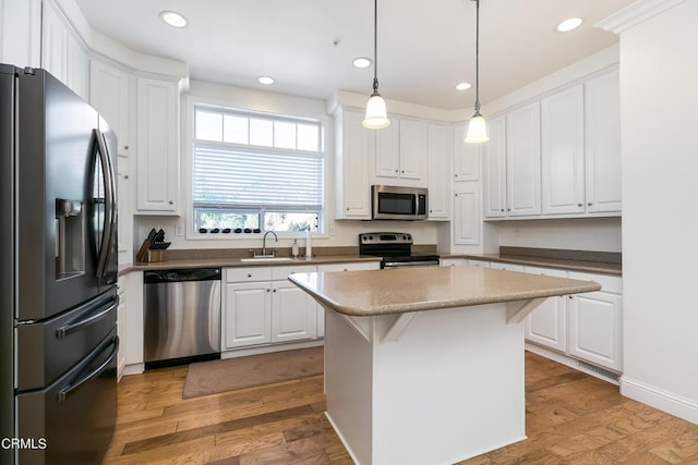 kitchen with appliances with stainless steel finishes, light hardwood / wood-style floors, a kitchen island, and white cabinets