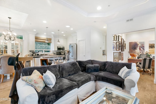 living room featuring a notable chandelier, light hardwood / wood-style flooring, crown molding, and a tray ceiling