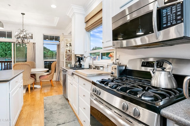 kitchen with light hardwood / wood-style floors, white cabinetry, stainless steel appliances, and a notable chandelier