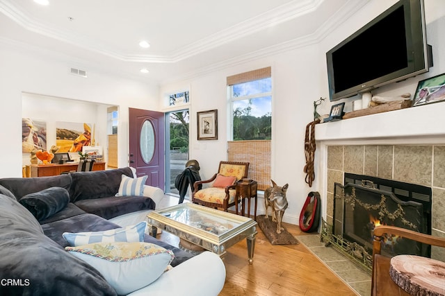 living room featuring light wood-type flooring, crown molding, a raised ceiling, and a tile fireplace