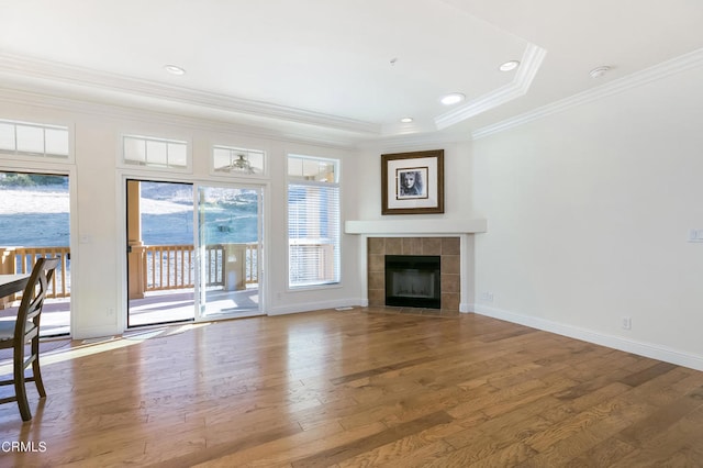 unfurnished living room featuring wood-type flooring, a fireplace, a tray ceiling, and ornamental molding