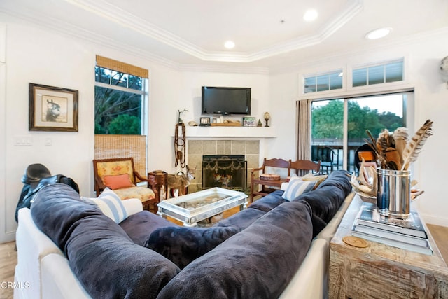 living room with ornamental molding, wood-type flooring, a tiled fireplace, and a tray ceiling