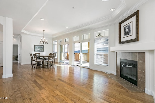 living room featuring an inviting chandelier, a fireplace, a raised ceiling, and light hardwood / wood-style flooring