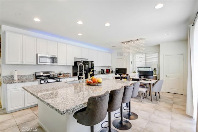 kitchen featuring light stone countertops, stainless steel appliances, a spacious island, sink, and white cabinets