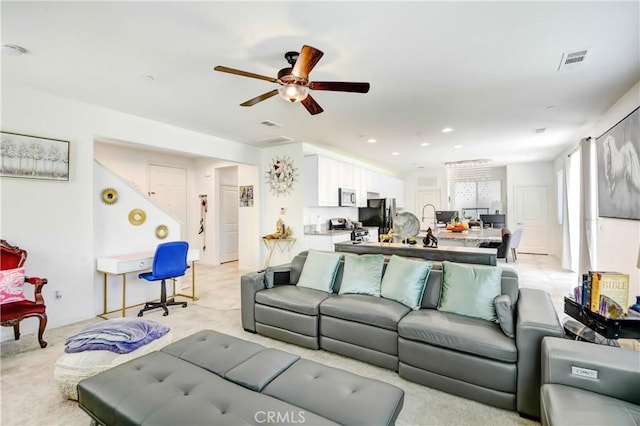 carpeted living room with ceiling fan and sink