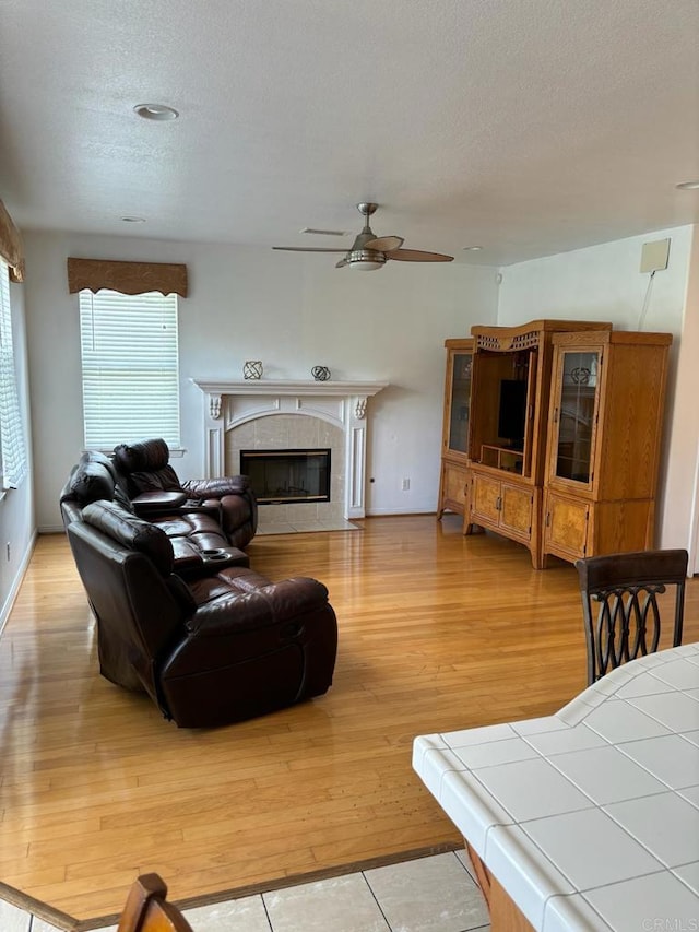 living room with ceiling fan, a textured ceiling, light wood-type flooring, and a fireplace