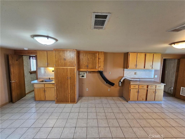 kitchen with light countertops, brown cabinetry, a sink, and visible vents