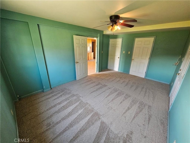 unfurnished bedroom with carpet floors, a ceiling fan, and multiple closets