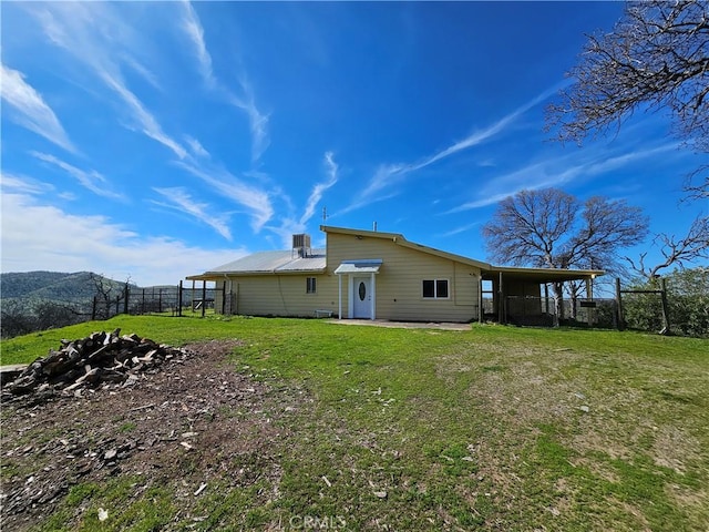 back of property with metal roof, a carport, a lawn, and fence