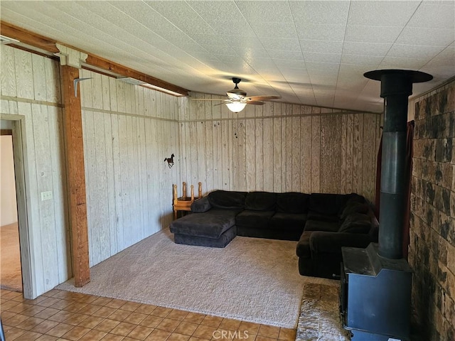 living room with carpet, a wood stove, ceiling fan, and wooden walls