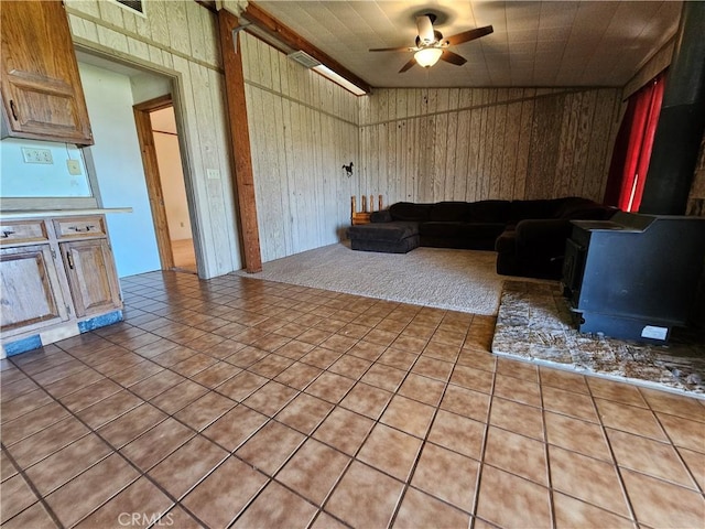 unfurnished living room with a ceiling fan, a wood stove, visible vents, and wooden walls