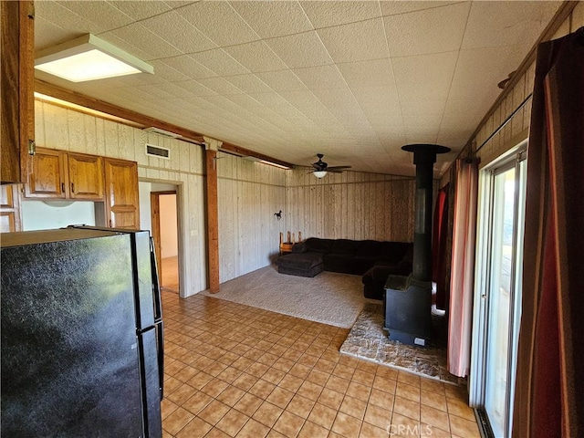 kitchen featuring brown cabinets, visible vents, freestanding refrigerator, a wood stove, and wooden walls