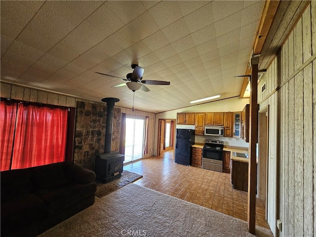 interior space with brown cabinetry, lofted ceiling, appliances with stainless steel finishes, a wood stove, and light countertops