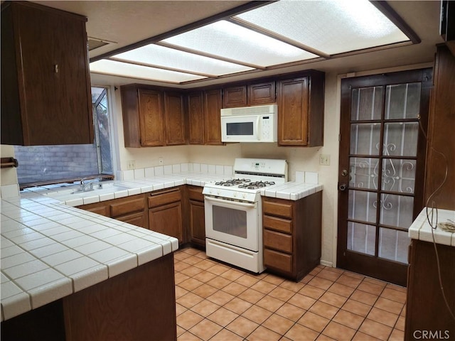 kitchen with kitchen peninsula, white appliances, sink, light tile patterned floors, and tile counters