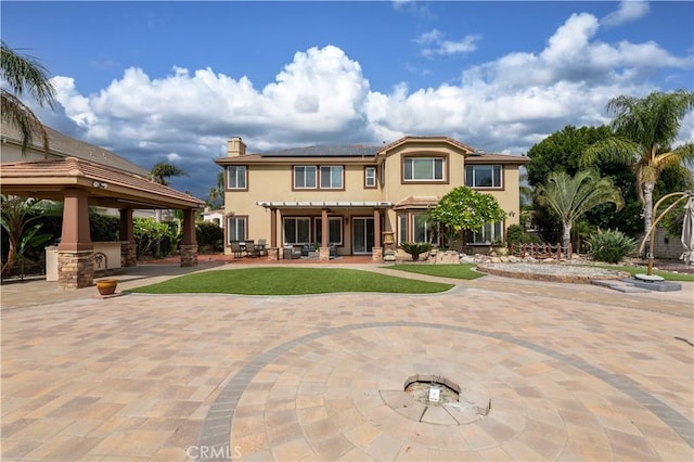 rear view of house featuring a lawn, a gazebo, an outdoor bar, solar panels, and a patio