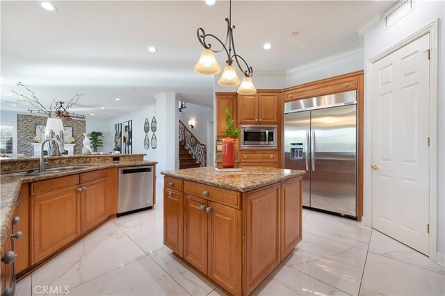 kitchen featuring decorative light fixtures, a kitchen island, sink, built in appliances, and light stone counters