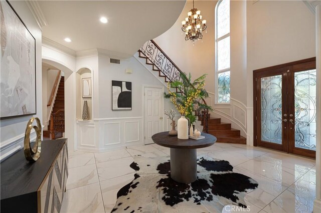 foyer with ornamental molding, a chandelier, and french doors