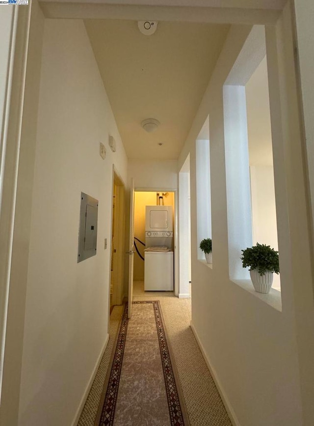 hall with electric panel, stacked washer / dryer, and light colored carpet