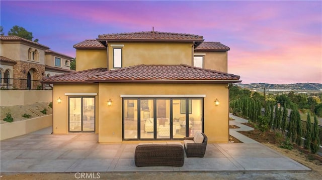 back house at dusk featuring a patio