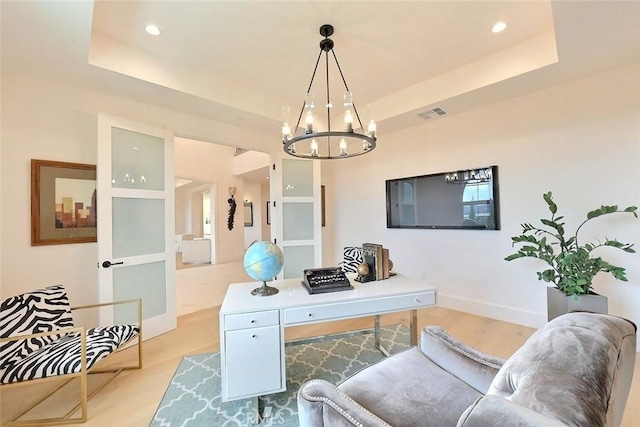 office with an inviting chandelier, light hardwood / wood-style floors, and a raised ceiling