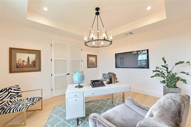 office featuring a raised ceiling, a notable chandelier, and light wood-type flooring