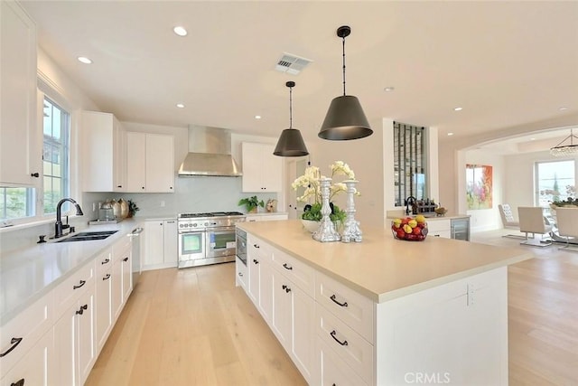 kitchen featuring sink, wall chimney exhaust hood, appliances with stainless steel finishes, a kitchen island, and white cabinetry